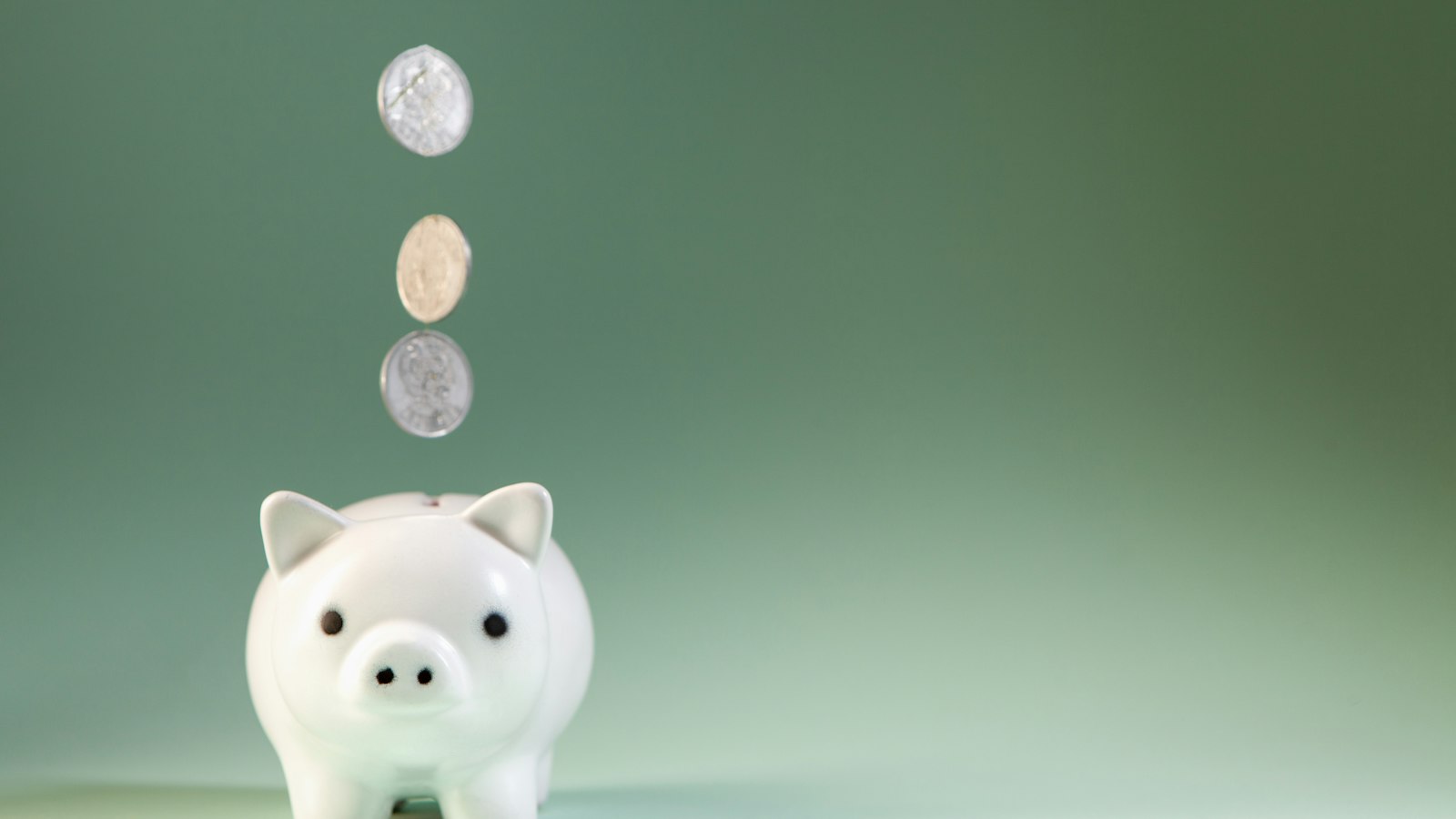Coins falling into a white piggy bank